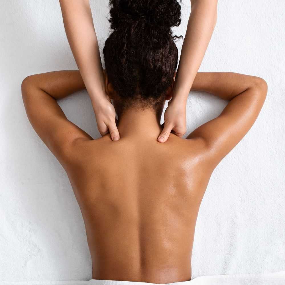 Person holding their neck, showing their bare back against a wall.