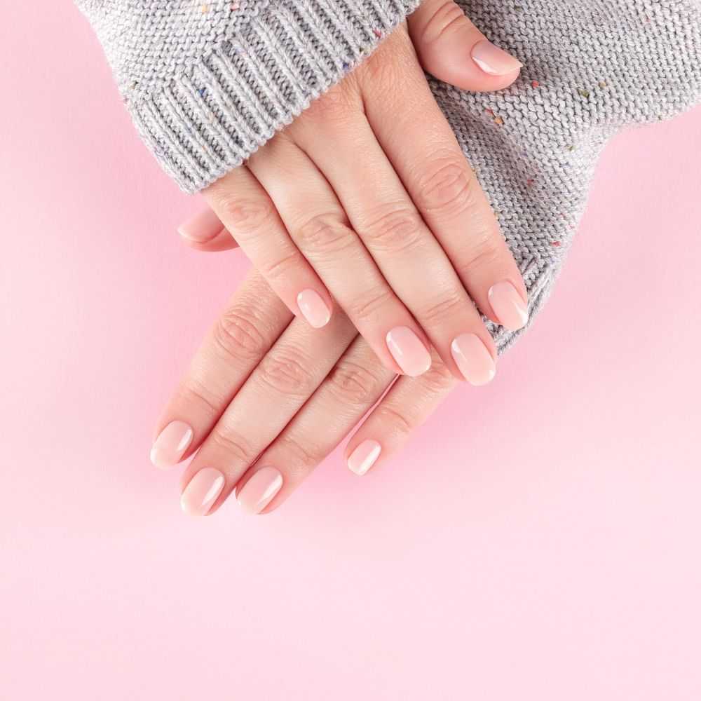 Hands with pink manicured nails on a pastel background.